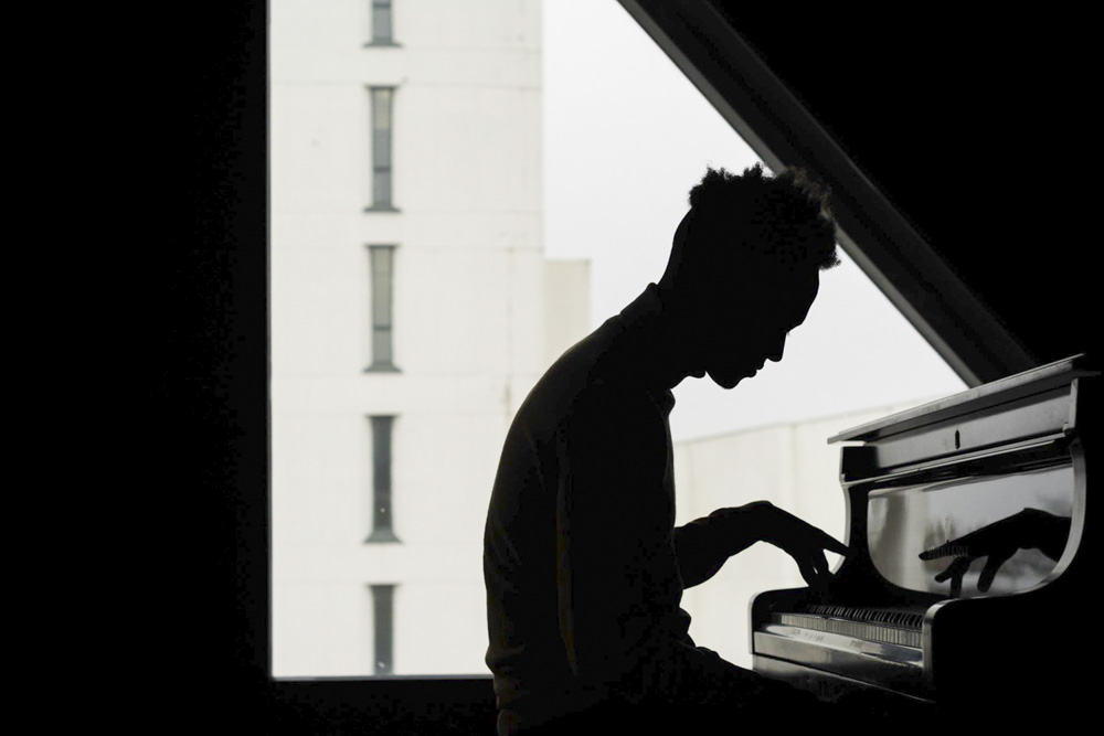 het is een liggend beeld waar een man voor een raam piano speelt. Het onderwerp is volledig gesilhouetteerd.